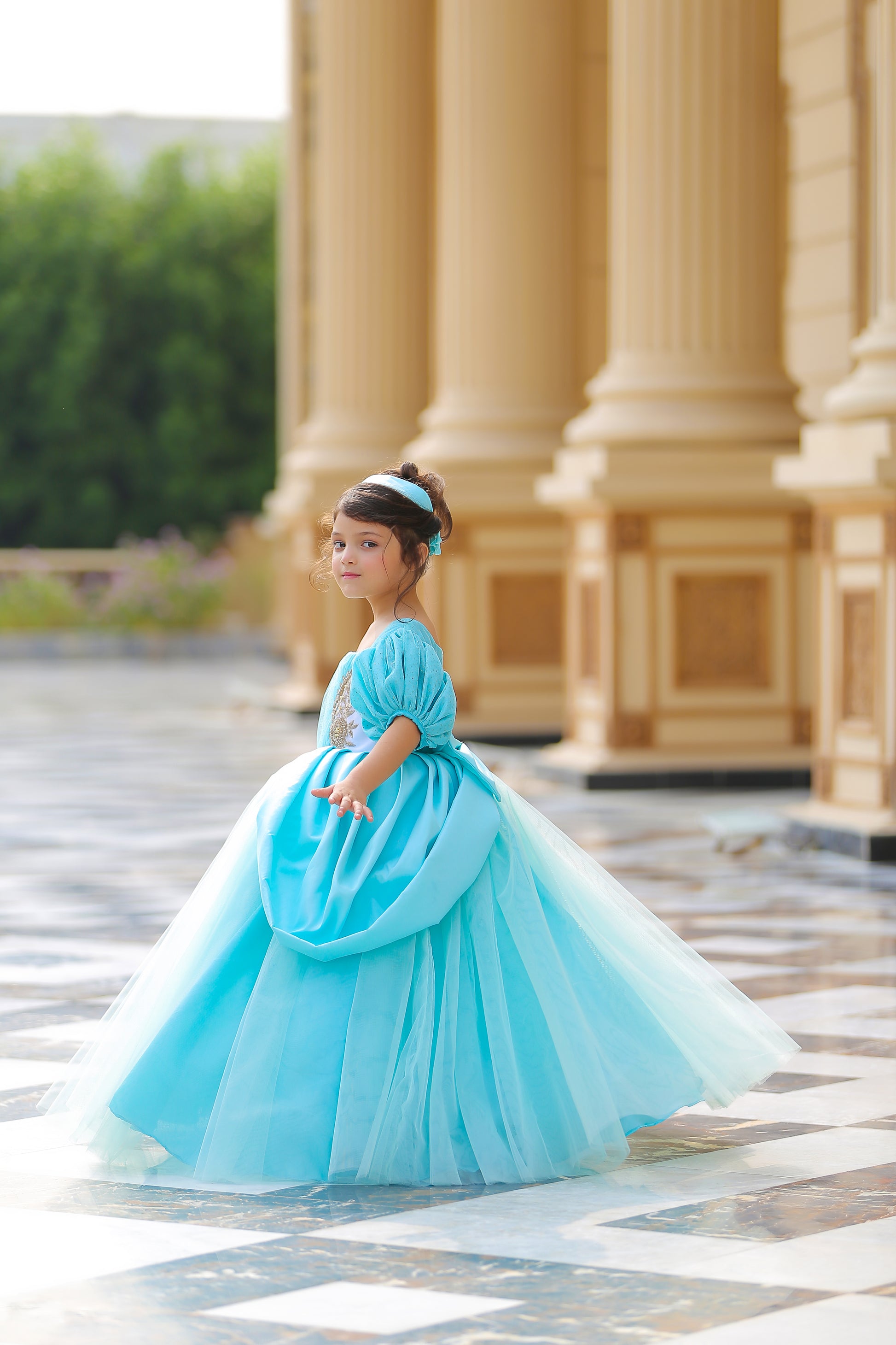 A young girl in a Cinderella costume with white and sky-blue colors, standing in a columned hallway.