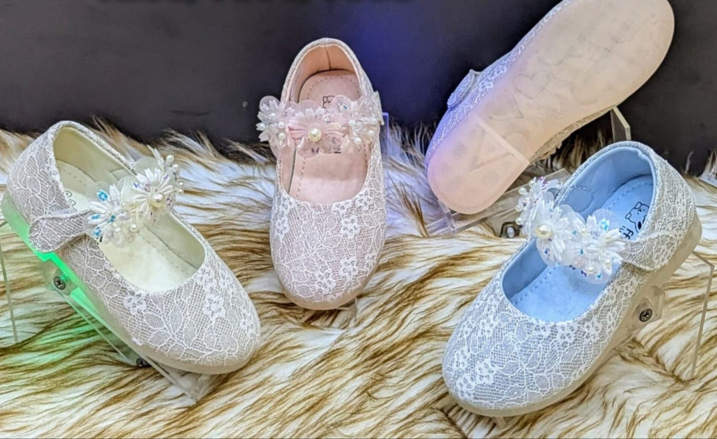 A pair of white baby shoes with decorative embellishments in powder pink and sky blue, presented on a furry surface.