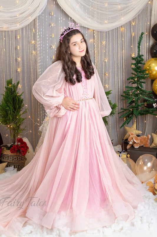 A person wearing a pink, floral, sleeveless, maxi dress with a sweetheart neckline, standing in a decorated room with Christmas trees and lights in the background.